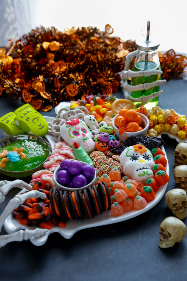Halloween-themed sweets shaped like pumpkins and ghosts arranged on a table with spooky decorations and cobwebs. The tone is fun and playful.