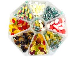 Assorted sugar-free sweets in various bright colors arranged in a decorative bowl on a clean white table. The sweets are organized in a tidy and inviting way, with soft daylight highlighting their glossy surfaces. The setting feels fresh and health-conscious, creating a sense of reassurance and care. No visible text.